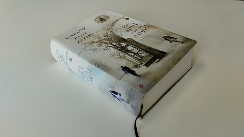 Tweedehands boek: Het spel van de engel van auteur Carlos Ruiz Zafón - In goede staat. Nederlandstalige hardcover met stofomslag en leeslint. Lichte gebruikssporen aan stofomslag, kaft en pagina’s netjes en schoon.