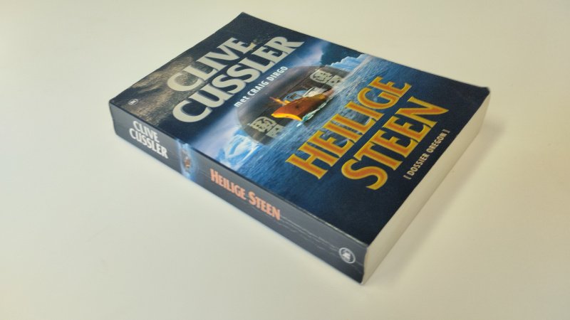Tweedehands boek: Heilige steen van auteur Clive Cussler - In goede staat. Nederlandstalige paperback met lichte gebruikssporen aan de kaft. Pagina's netjes, onbeschreven en goed in de binding.