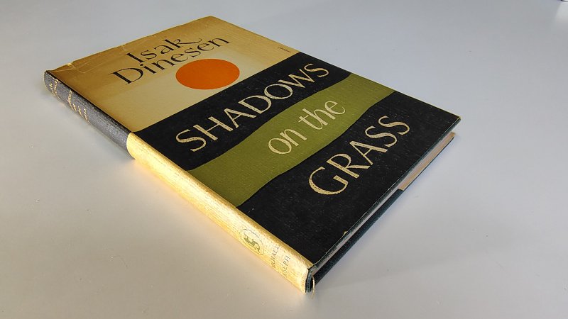 Tweedehands boek: Shadows on the Grass van auteur Isak Dinesen pseudoniem van Karen Blixen - Engelstalige hardcover met stofomslag. De omslag verkleurd en versleten. De donkergroene linnen kaft met goudopdruk is nog goed. Binnenwerk onbeschreven en zeer netjes.